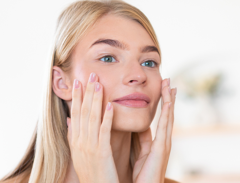 Frau mit langen, blonden Haaren berührt sanft ihr Gesicht.